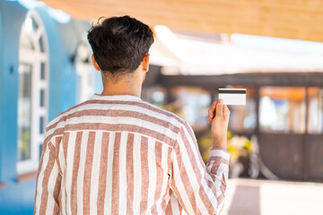Handsome Arab man holding a credit card at outdoors in back position