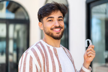 Handsome Arab man holding invisible braces at outdoors smiling a lot