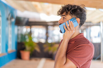 Young Arabian handsome man at outdoors keeping a conversation with the mobile phone with someone