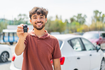 Young Arabian handsome man holding car key at outdoors with happy expression