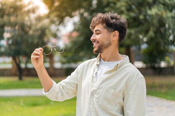 Young Arabian handsome man with glasses at outdoors with happy expression