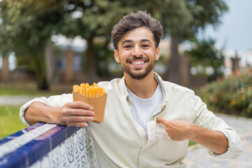 Young Arabian handsome man holding fried chips at outdoors with surprise facial expression