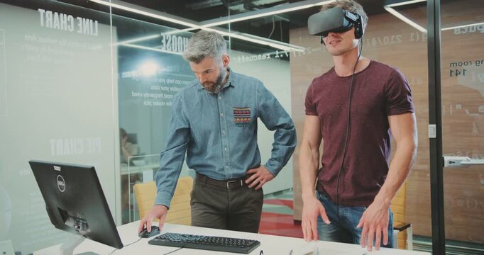 NEW YORK - April 5, 2017:Two handsome scientists testing virtual reality glasses in science centre. Guy talking about feelings. Programmer recording impressions in computer. Indoor.