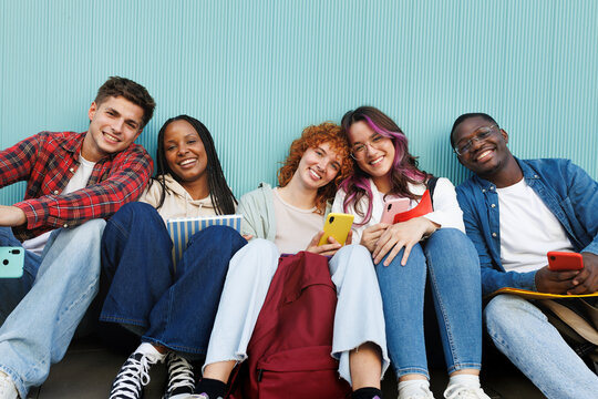 Happy students using mobile phones and relaxing together outdoors