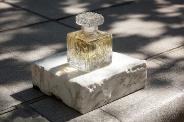 Clear glass perfume bottle, light gold liquid, on a white stone pedestal