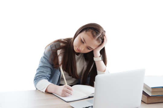 Serious Caucasian girl learning online with laptop and writing homework on notebook in classroom of school. Education cancept