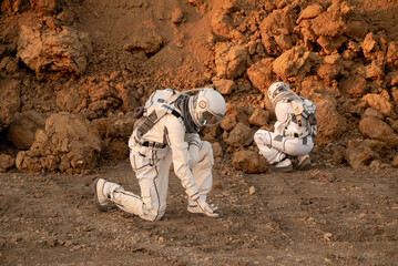 Two astronauts are exploring an alien planet, carefully examining a rock sample they have picked up from the surface. © Tetiana Tuzyk