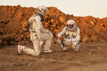 Two astronauts are exploring an alien planet, carefully examining a rock sample they have picked up from the surface.