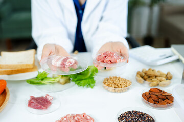 Female scientist in lab coat and goggles examining raw meat with tweezers in food lab. Nutrition, protein, food safety, and research concept.