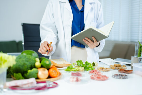 Female nutritionist in lab coat analyzing food and writing in notebook. Healthy eating, organic testing, and nutrition science in a clean lab.