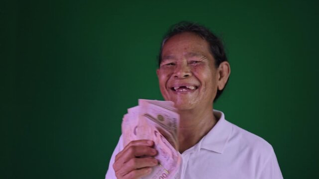 Happy elderly Asian woman holding money Thai baht banknotes with big smile, Financial success, luck, and retirement joy on chroma key green screen background, Grandmother happily with a money