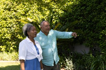 Walking in lush green garden, African American senior couple smiling warmly