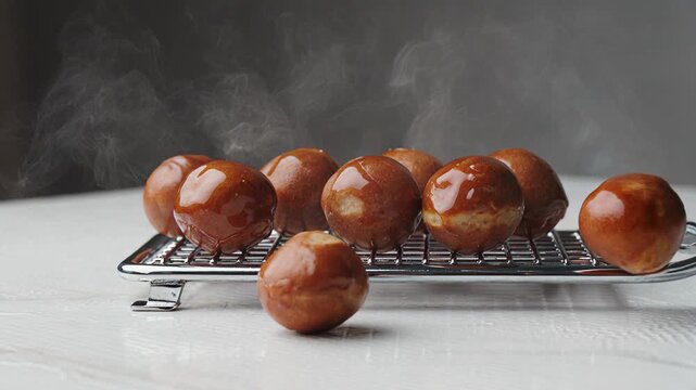 A batch of freshly baked steaming hot donut holes with a sweet sugar glaze resting on a wire cooling rack in a bright kitchen