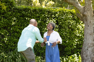 African American senior couple laughing and dancing together in sunny garden