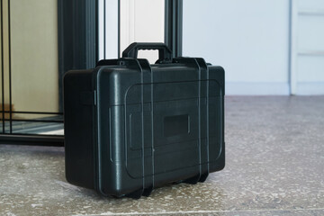 Black hard plastic tool case standing on floor near open apartment door, concept of repairman home visit or maintenance service. Photo