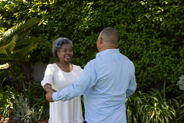 Senior couple dancing joyfully in garden, surrounded by lush greenery © wavebreak3