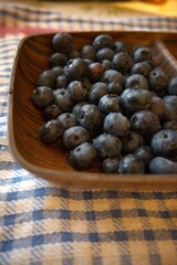 Close-up of blueberries on a wooden plate, set on a blue checkered cloth. Healthy snack, rustic food styling.