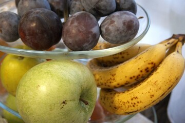 Close-up of fresh plums arranged in a transparent glass serving bowl. Healthy fruit concept.