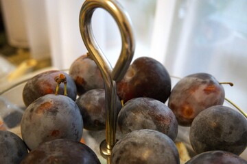 Close-up of fresh plums arranged in a transparent glass serving bowl. Healthy fruit concept.