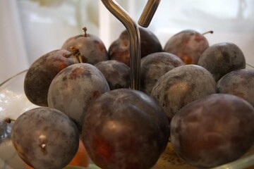 Close-up of fresh plums arranged in a transparent glass serving bowl. Healthy fruit concept.