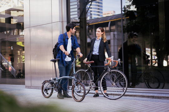 Commuting to work with bicycle. Businessman businesswoman cycling to office in downtown district. Modern diverse people use eco transportation on city street. Environmental pollution, climate change.