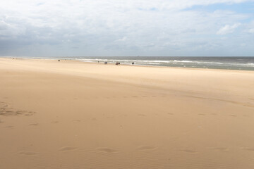 Wide sandy beach with people walking along the shore under a cloudy sky in the afternoon