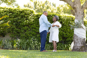 Senior couple dancing joyfully together in sunny garden, enjoying outdoor moment