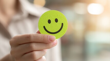 Close up photo of hand holding bright green smiley face sticker with blurred background, soft natural light and shallow depth of field, symbolizing positivity and support for World Mental Health Day