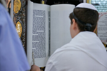 A bar mitzvah boy reading from the Torah scroll in a synagogue.