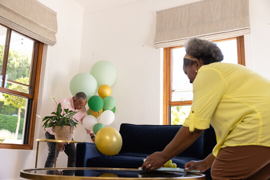 Decorating living room, senior couple arranging balloons and table for celebration - Powered by Adobe