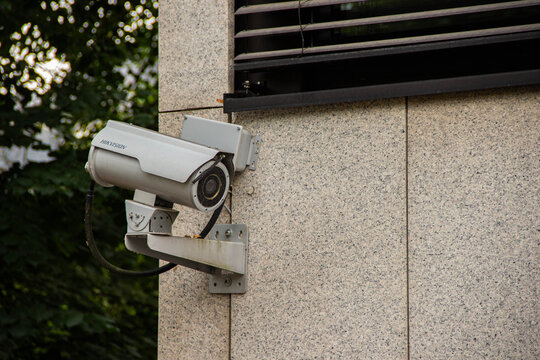 Security camera mounted on a textured stone wall, capturing surveillance footage, surrounded by greenery, emphasizing safety and monitoring in urban environments