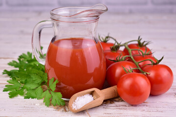Decanter with tomato juice on white wooden background.
