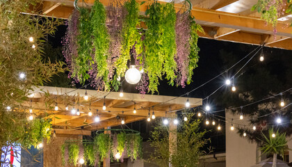 Creative ceiling decoration featuring green and purple hanging plants with a glowing light bulb