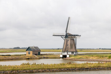 Fototapeta premium Traditional windmill stands majestically beside a serene pond, surrounded by lush green fields and a quaint house, showcasing rural tranquility. free space