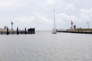 Sailboat navigating through calm waters towards harbor entrance, surrounded by green and red navigation lights, showcasing maritime tranquility. free space