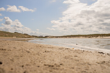 Coastal landscape with gentle waves and sandy shore under a partly cloudy sky at a tranquil beach location