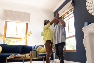 Senior couple dancing joyfully at home in living room, celebrating together