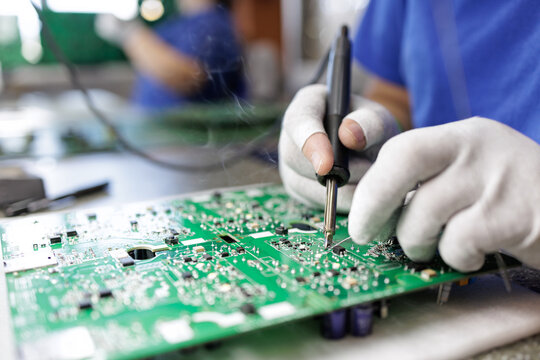 Gloved technician hand soldering components on printed circuit board in factory