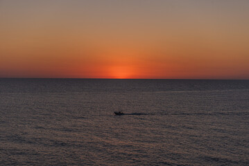 A boat drifting on calm waters at sunrise or sunset.