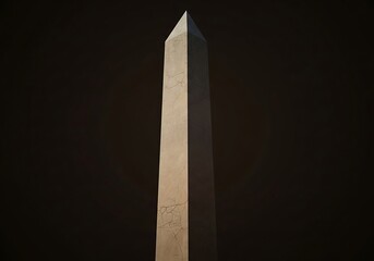 Monumental stone obelisk stands tall against a deep shadowy backdrop