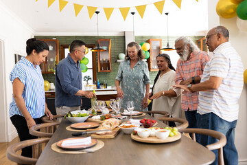 Gathering around dining table, senior friends preparing meal and having conversation