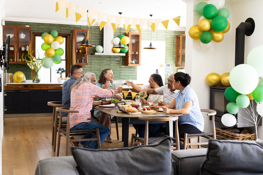 Senior friends celebrating together at home, raising glasses around festive table - Powered by Adobe