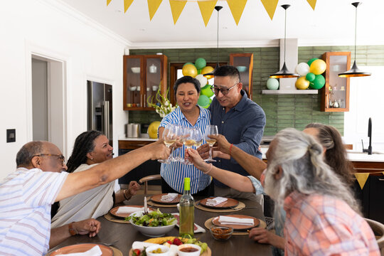 Senior friends toasting with wine glasses at home during festive party - Powered by Adobe