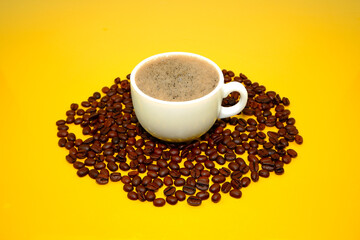 A cup of coffee with coffee beans closeup view on yellow background 
