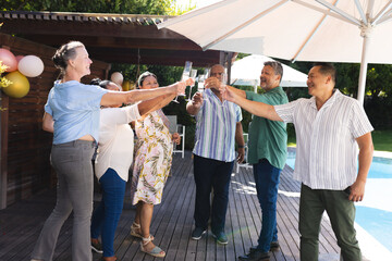 Seniors celebrating outdoors, raising glasses in joyful toast by poolside