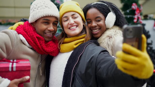 Multicultural friends capturing joyful moment while taking selfie during festive christmas market gathering with holiday spirit and urban winter backdrop