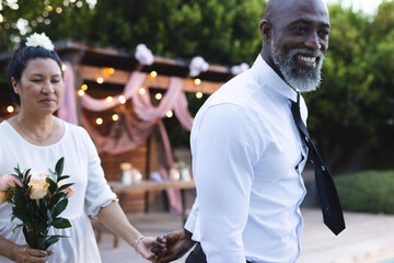 Holding hands, senior couple with flowers celebrating special occasion outdoors