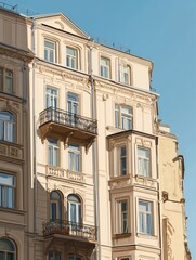 Obraz premium A sunlit, tan multi-story building with ornate details, including balconies and bay windows, against a clear blue sky. The architectural style suggests a historical European influence