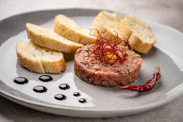 Beef tartare with egg yolk, bread slices, and chili pepper on a plate