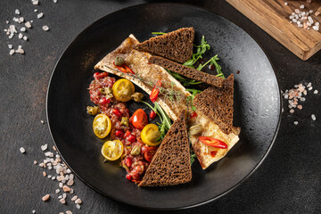 Gourmet roasted bone marrow with bread, tartare, and vegetables on a black plate
